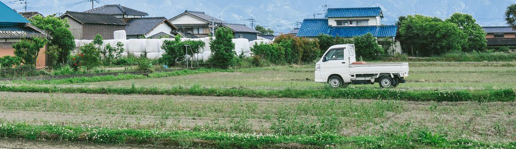 集落のそばの畑に止まる白い軽トラ